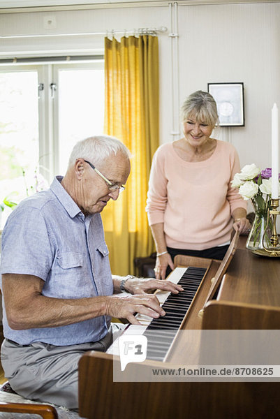 Senior man playing piano while woman looking at him indoors