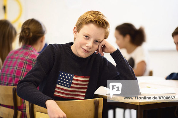 Porträt eines selbstbewussten Schülers am Schreibtisch im Klassenzimmer
