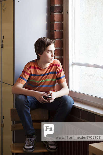 Thoughtful boy looking out through window in locker room at school