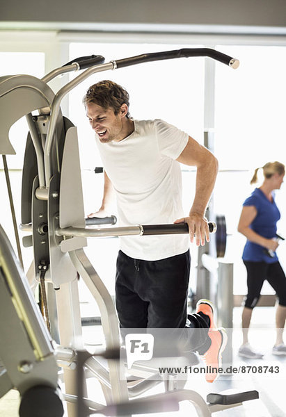 Mann trainiert an der Klimmzugmaschine im Fitnessstudio