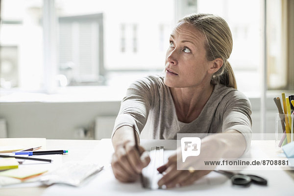 Businesswoman drawing line using ruler on paper while looking away