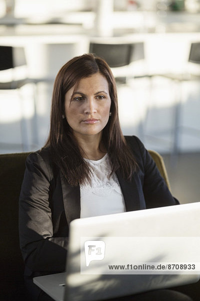Businesswoman with laptop looking away while sitting in office