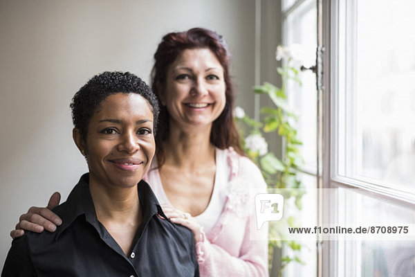 Portrait of smiling lesbian couple by window at home