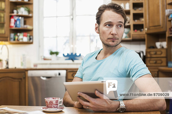Mann hält digitales Tablett  während er in der Küche wegschaut.