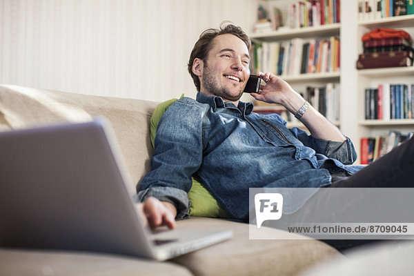 Man on call while using laptop on sofa at home