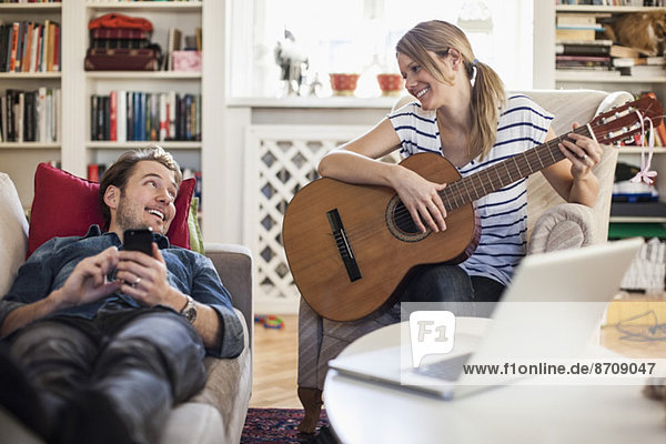 Happy woman playing guitar for man at home
