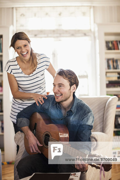 Glücklicher Mann spielt Gitarre für Frau im Haus