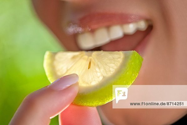 Woman holding slice of lime to mouth