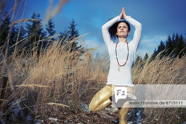 Mittlere erwachsene Frau macht stehende Baum-Yoga-Pose im Wald