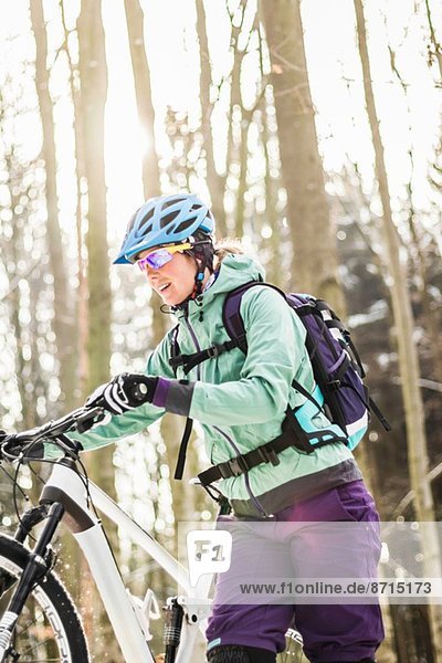 Mid adult female mountain biking pushing bike through forest