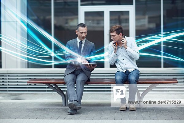 Geschäftsmann und junger Mann beim Betrachten von digitalen Tabletts und Beleuchtungswellen