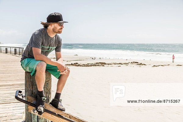 Young man sitting on wooden post  Laguna Beach  California  USA