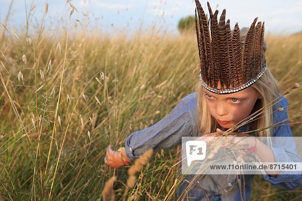 Girl hiding in long grass dressed up as a native american