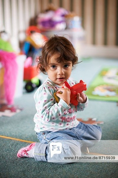 Kleinkind auf dem Spielzimmerboden sitzend mit rotem Spielzeug spielend