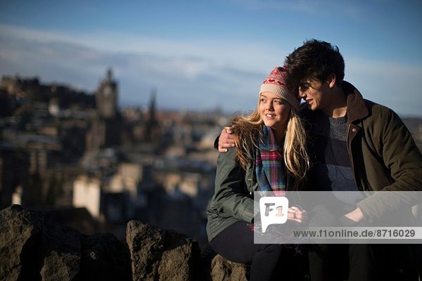 Ein junges Paar umarmt sich auf Calton Hill mit dem Hintergrund der Stadt Edinburgh  der Hauptstadt Schottlands.