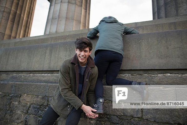 Ein junger Mann hilft seiner Freundin auf das National Monument am Calton Hill in Edinburgh  Schottland.