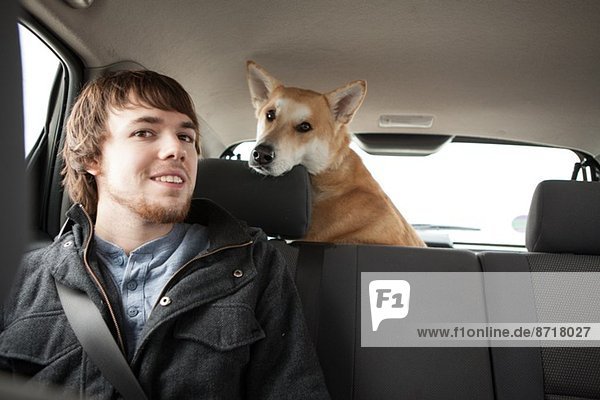 Junger Mann und sein gekreuzter Schäferhund im Autositz