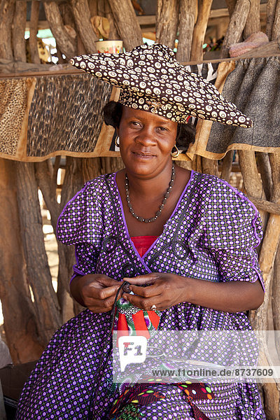 Herero-Frau mit typischer Kopfbedeckung beim Nähen von Souvenirs  Namibia