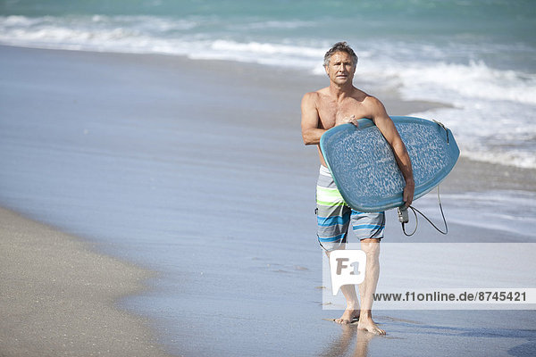 Mature Man Walking down Beach with Surfboard  USA