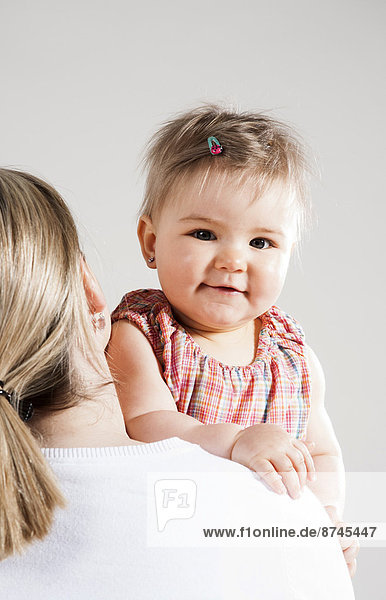 Portrait of Baby Girl Looking over Mother's Shoulder  Studio Shot