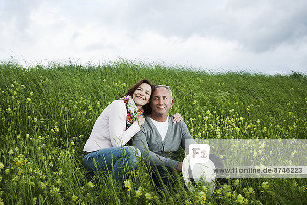 Portrait of mature couple sitting in field of grass  embracing  Germany