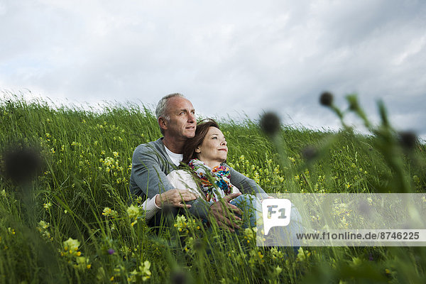 Mature couple sitting in field of grass  embracing  Germany