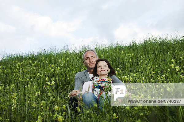 Portrait of mature couple sitting in field of grass  embracing  Germany