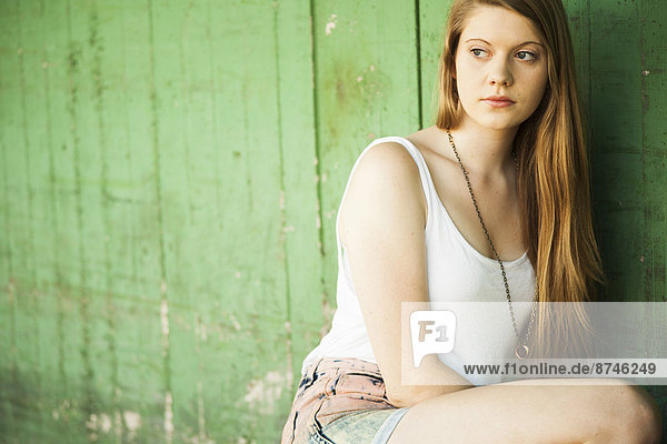Portrait of young woman outdoors  crouching down by wall  looking to the side