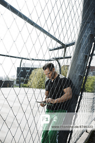 Mature man standing on outdoor basketball court looking at tablet computer  Germany