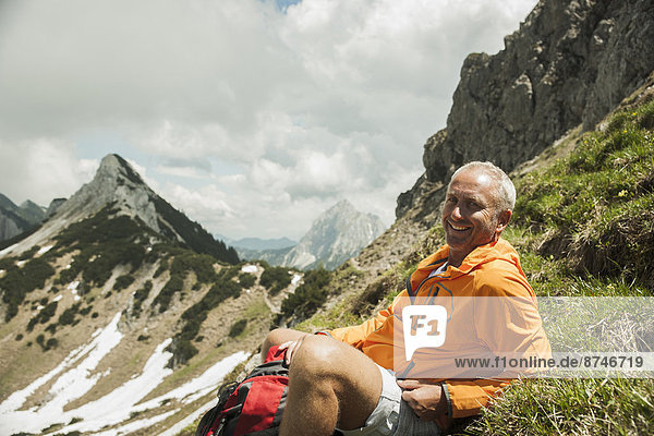 Portrait of mature man sitting on grass  hiking in mountains  Tannheim Valley  Austria
