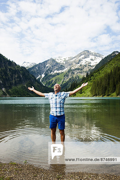 Mature man with arms stretched outward  standing in Lake Vilsalpsee  Tannheim Valley  Austria
