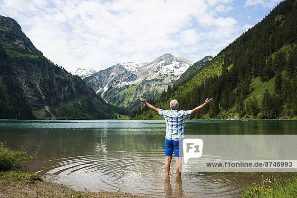 Backview of mature man with arms stretched outward  standing in Lake Vilsalpsee  Tannheim Valley  Austria