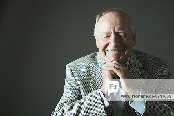 Portrait of senior man smiling with eyes closed  studio shot on grey background