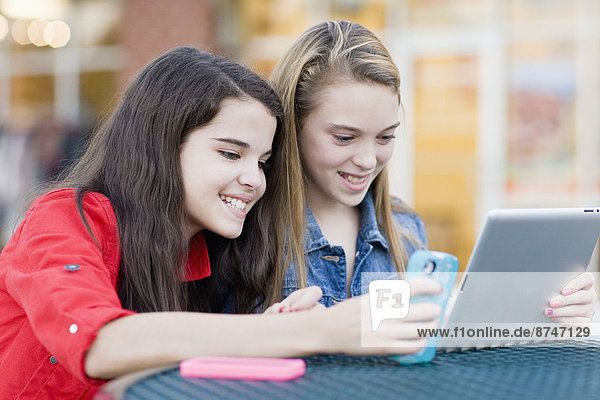 Girls using Cell Phone and Tablet Computer at Outdoor Cafe  USA