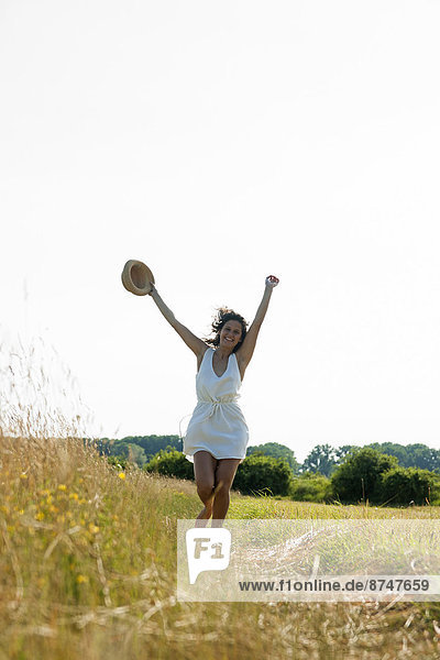 Teenaged girl holding straw hat with arms in air  walking in field on a summer day  Germany