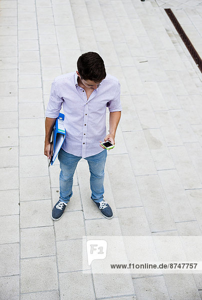 High angle view of young man standing outdoors  looking at cell phone  Germany