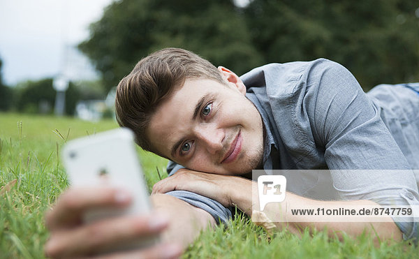 Close-up of young man lying on grass  looking at cell phone  Germany