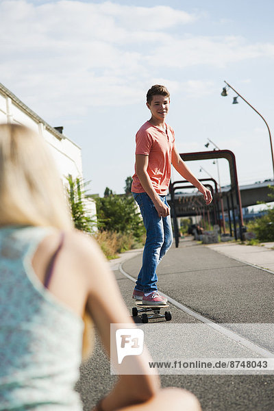 Backview of teenage girl in foreground and teenage boy on skateboard in background  Germany
