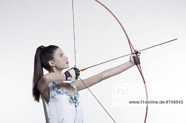 Side view of young  woman archer  aiming bow and arrow  studio shot on white background