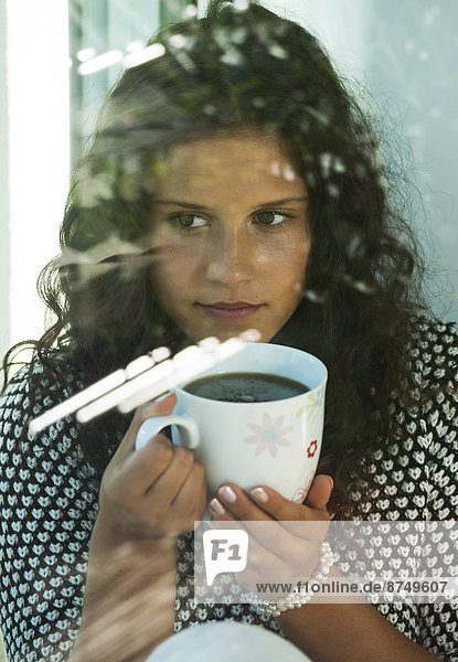 Teenage girl sitting next to window  holding cup in hands  Germany