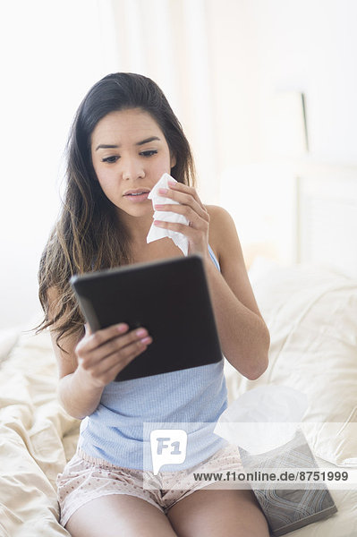 Hispanic woman holding tissue and using digital tablet in bed
