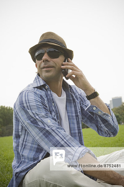Hispanic man talking on cell phone in grass at park