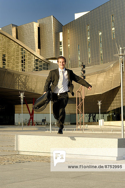 Businessman jumping bench in front of modern office building