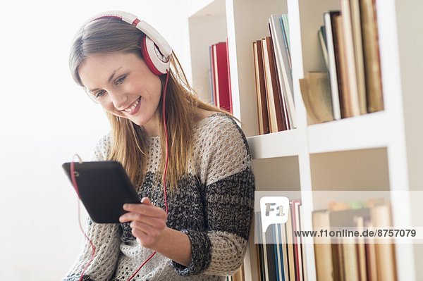 Young woman sitting on floor and listening to music on digital tablet