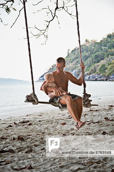 Father with baby swinging on beach  Thailand
