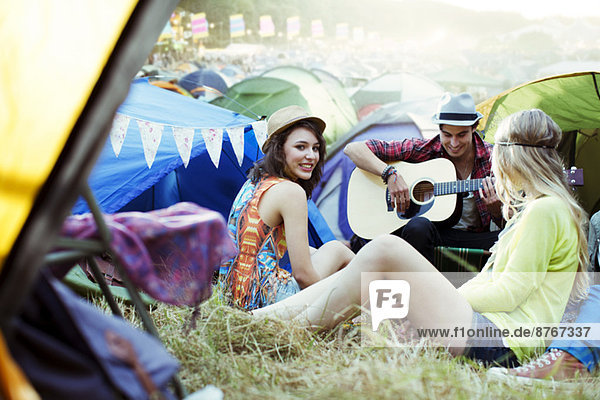 Friends with guitar hanging out near tents at music festival