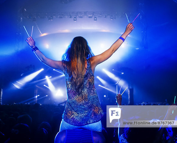 Cheering woman with glow sticks on manÍs shoulders at music festival