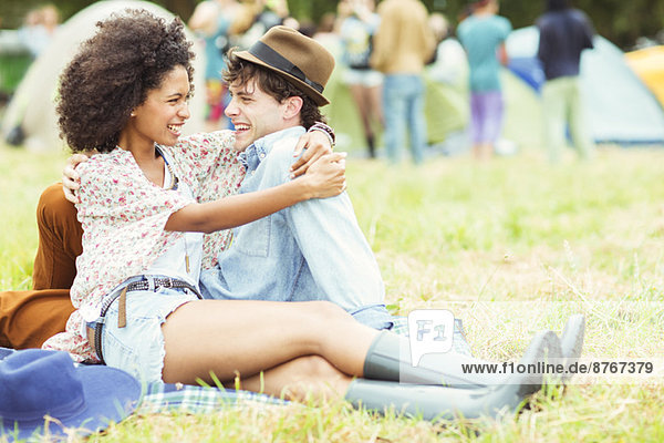 Couple hugging in grass outside tents at music festival
