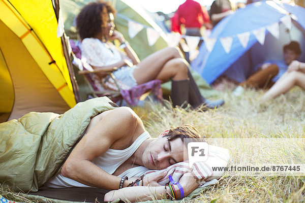 Mann schläft im Schlafsack vor dem Zelt beim Musikfestival