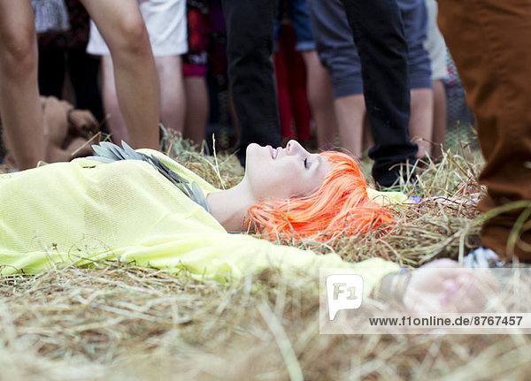 Woman in wig laying with arms outstretched in grass at music festival